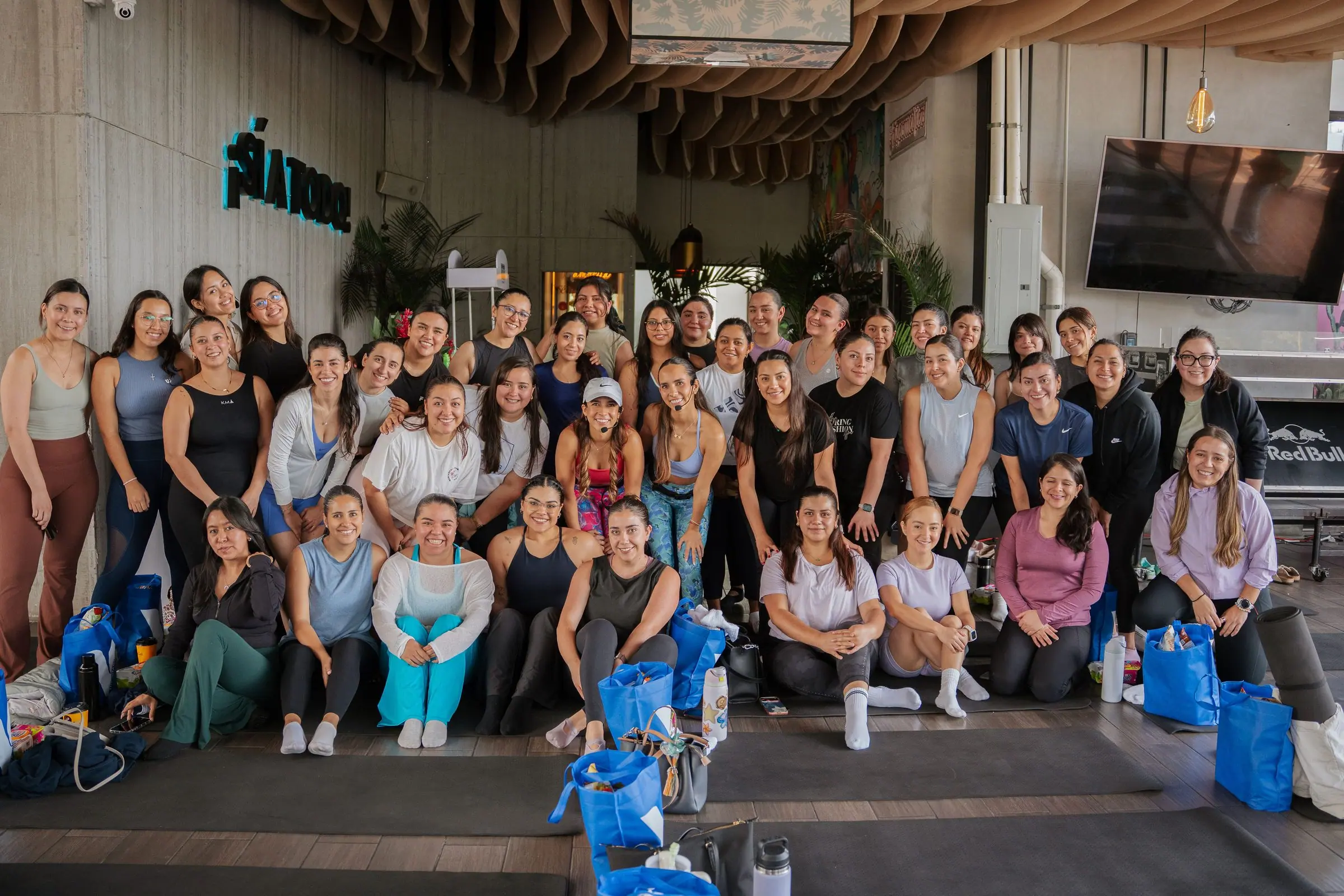 Foto grupal de todas las asistentes del evento Pilates & Charms en el rooftop, de pie y sentadas en los tapetes, todas sonriendo a cámara