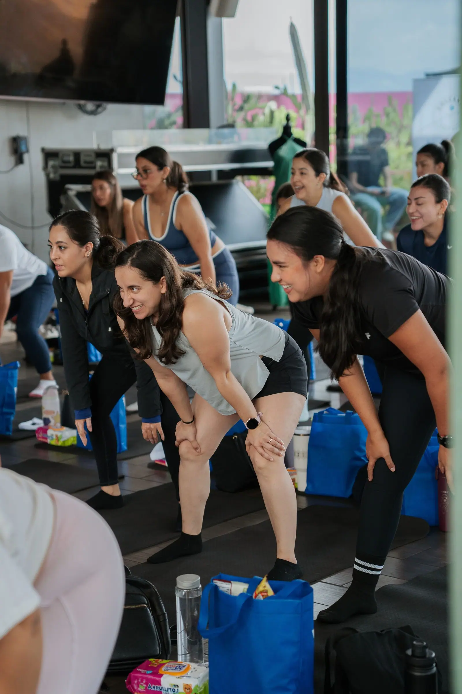 Clase en rooftop: asistentes inclinadas con las manos en las rodillas, riéndose en medio del ejercicio